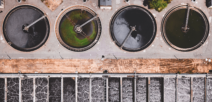 An aerial view of a water treatment plant with circular tanks and rectangular sedimentation basins.