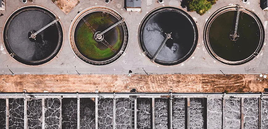 An aerial view of a water treatment plant with circular tanks and rectangular sedimentation basins.