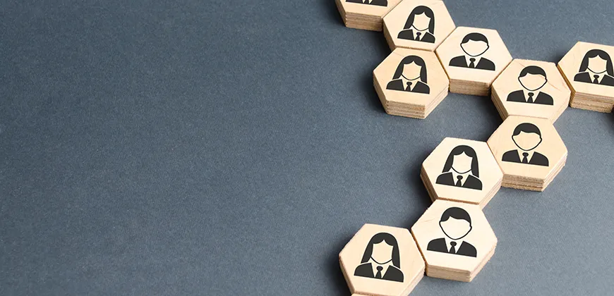 A group of wooden hexagonal blocks arranged in a honeycomb pattern on a dark background. Each block has a black silhouette of a person on it, representing a network or team.