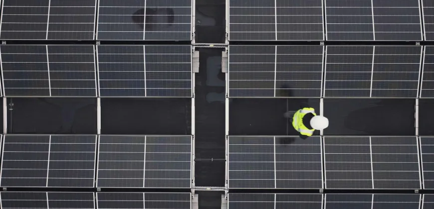 A person wearing a hard hat and safety vest walking across a large field of solar panels on a rooftop.